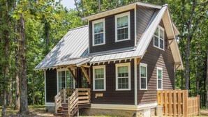 Une cabane à deux étages, dotée d’un toit en pente, d’une terrasse en bois et d’un petit escalier menant à l’entrée.