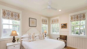 Une chambre à coucher avec un grand lit, deux tables de chevet, une chaise et un ventilateur de plafond.