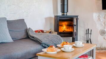 A cozy living room with a sofa, a table with pastries and cups, and a wood-burning stove.