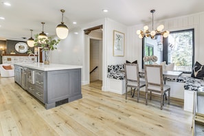A modern kitchen with a central island, pendant lighting, and a dining area with chairs and a table.