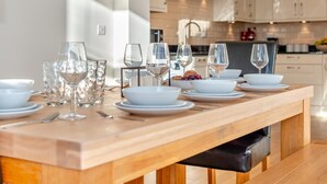 A modern kitchen with a wooden dining table set for a meal, equipped with white plates, bowls, and wine glasses. - 5 Bed in Mitchell (oc-c30790) (Mitchell)