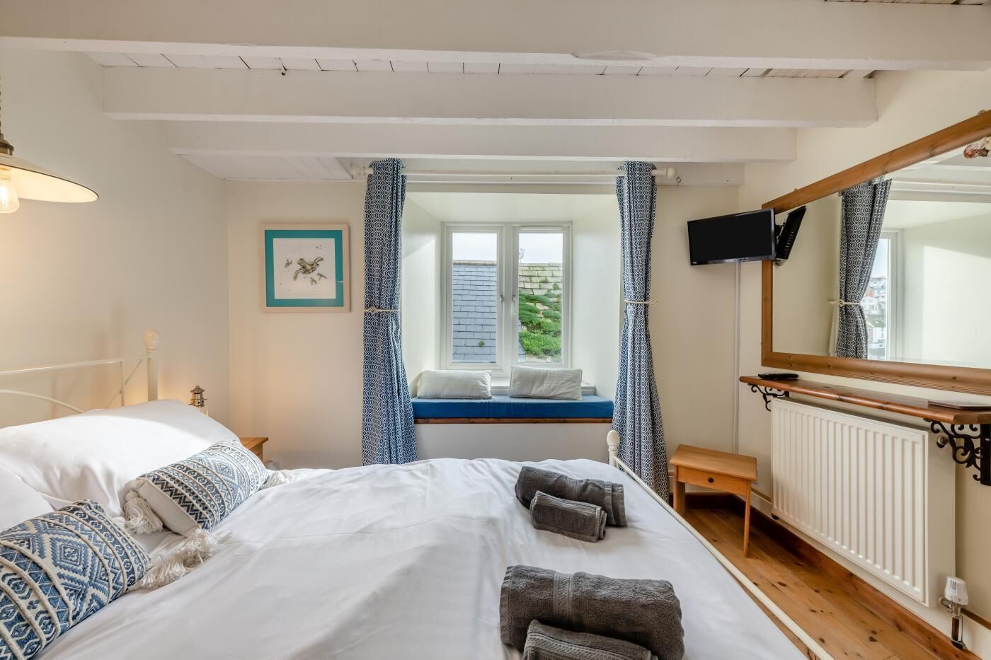 A bedroom with a bed, a window with a view, a bedside table, and a TV mounted on the wall.