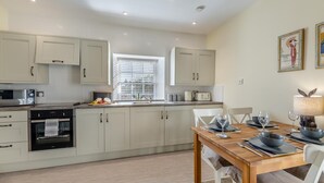 Een moderne keuken met witte kasten, een eettafel gedekt voor vier personen, en een raam met zonwering.