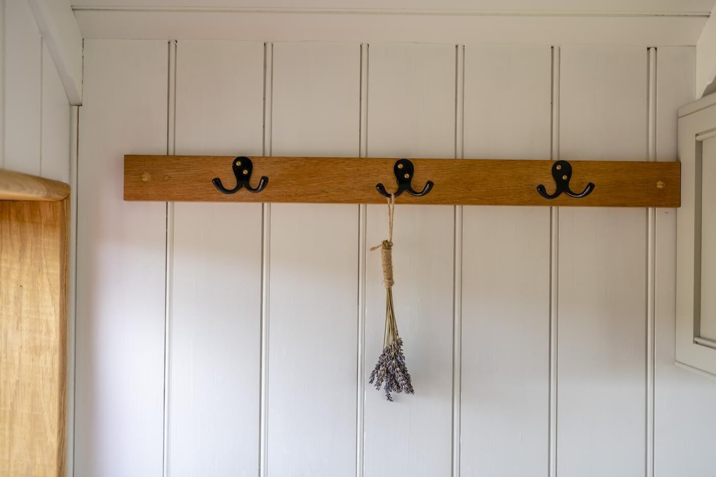 Ein hölzerner Kleiderhaken mit drei Haken an einer weißen Wand.