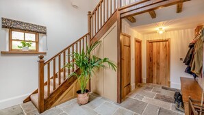 Eine Holztreppe führt zu einer zweiten Etage, eine Topfpflanze, Steinböden und ein Kleiderständer mit Jacken.