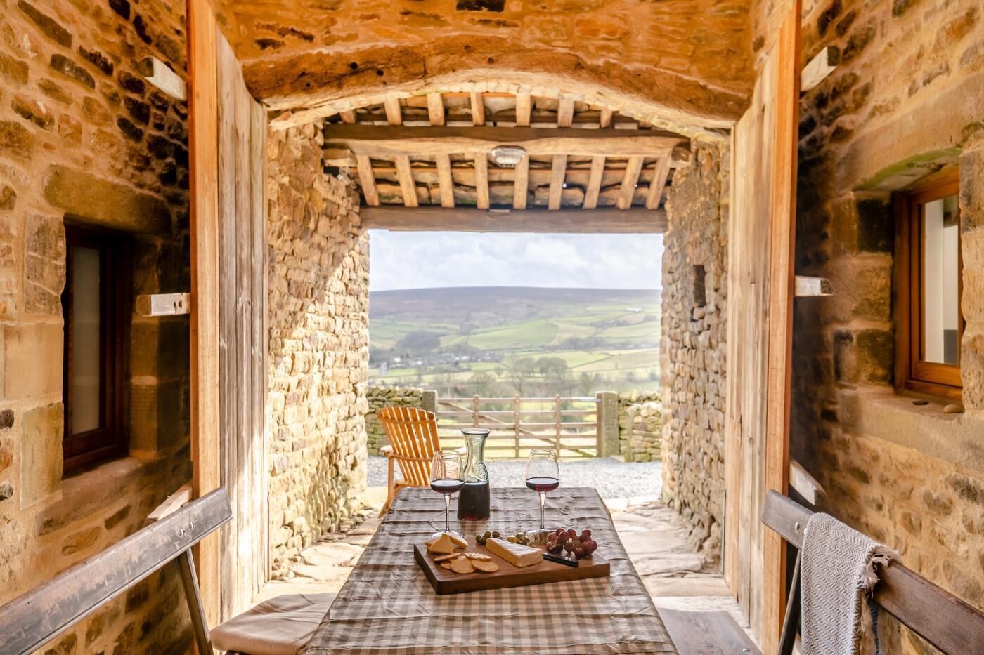 Una estança rústica de pedra amb una taula preparada per a dinar, vista al camp i sostre de fusta.