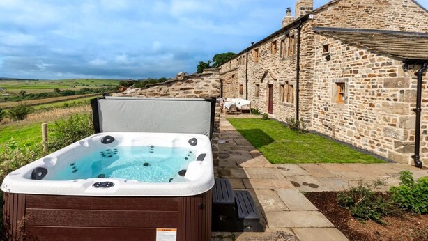 Ein Whirlpool vor einem Steinhaus mit einer Rasenfläche und blauem Himmel.