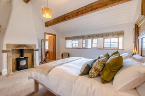A bedroom with a large bed, a fireplace, and a view of the sea through the windows. - 4 Bed in Cowling (oc-h30773) (Cowling)