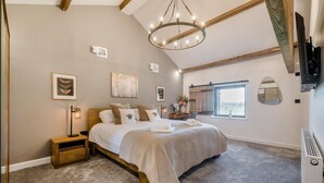 Quarto com uma cama grande, um candelabro, uma janela com vista e uma televisão na parede.