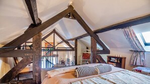 Une chambre à coucher aménagée dans un espace ouvert avec des poutres apparentes, un lit avec une literie à motifs, un escalier et une vue sur l’extérieur.