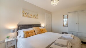 Un dormitorio ordenado con una cama grande, mesitas de noche, una lámpara de noche, un candelabro, un armario y una obra de arte floral en la pared.