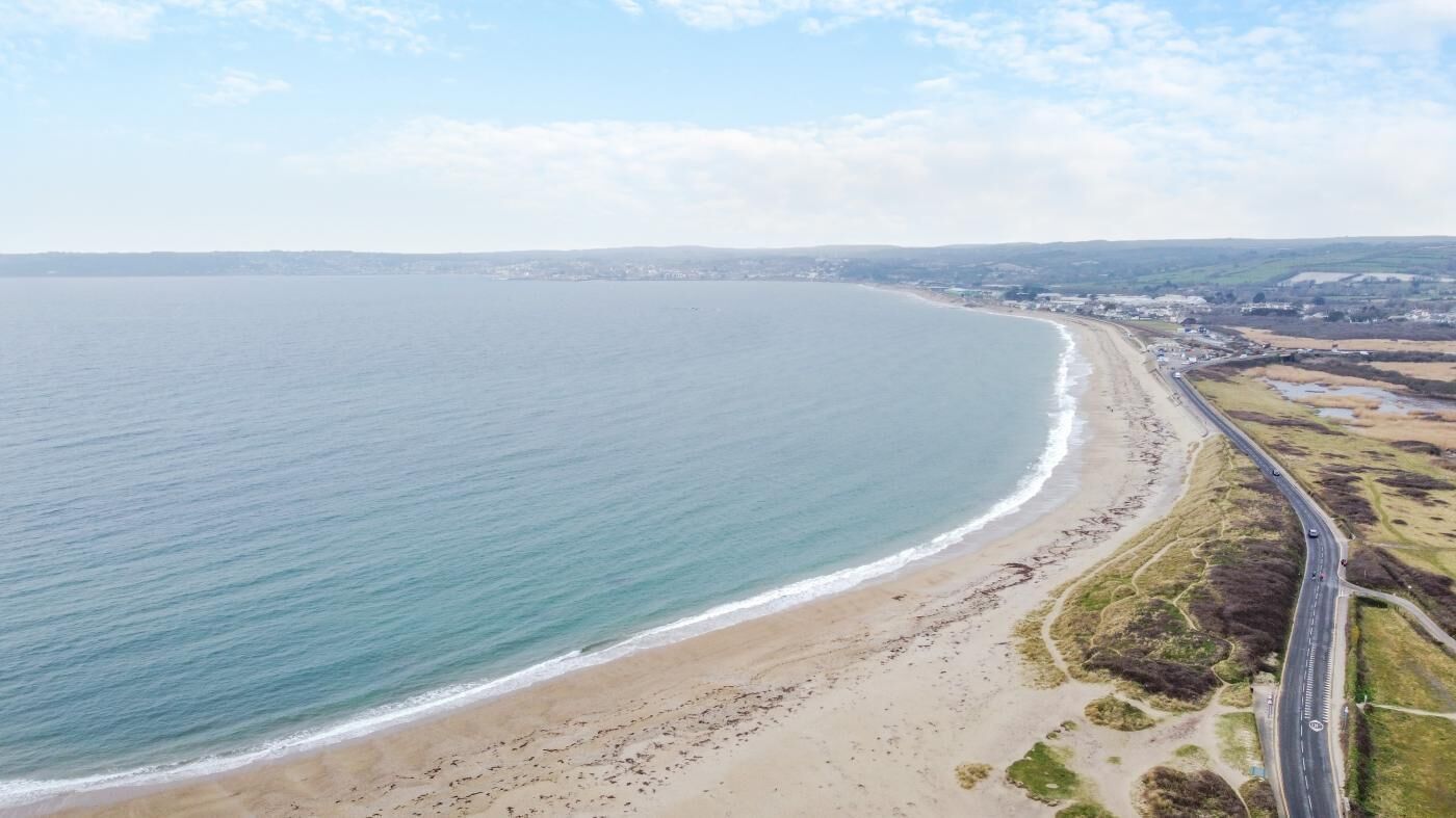 Vista aérea de una zona costera con playa, carretera y edificios a lo lejos.
