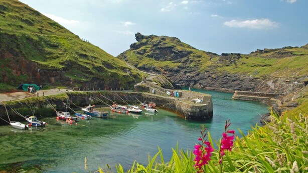 Un puerto con barcos amarrados, un muelle de piedra y una colina cubierta de hierba al fondo.