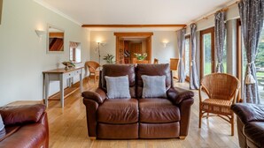 Una sala de estar con un sofá de cuero marrón, un sillón de mimbre, una mesa de comedor y una escalera que lleva a un piso superior.