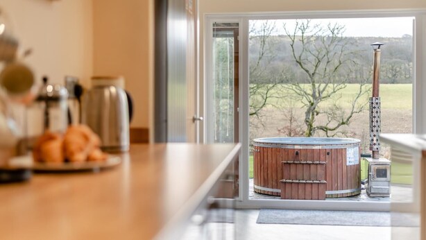 Una cucina moderna con un piano di lavoro in legno, una vasca idromassaggio e vista su un paesaggio rurale attraverso una porta vetrata.