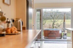 A modern kitchen with a wooden countertop, a hot tub, and a view of a rural landscape through a glass door. - 3 Bed in Isel (oc-i30816) (Setmurthy)