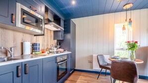 A modern kitchen with grey cabinets, stainless steel appliances, and a wooden countertop. There is a dining area with a table and chairs, and a window with a view of greenery. - 1 Bed in Newport (oc-f30846) (Newport)