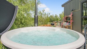 A hot tub outdoors with a chimney, surrounded by greenery and a wooden deck with a barbecue. - 1 Bed in Newport (oc-f30846) (Newport)