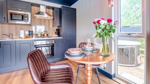A modern kitchen with dark cabinets, a stainless steel oven, and a microwave. There is a dining table with plates and a vase of flowers. - 1 Bed in Newport (oc-f30846) (Newport)