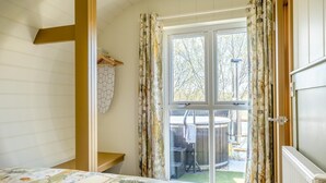 Et soveværelse med en seng, en træbænk, et vægmonteret knagered og en skydedør til en terrasse med et spabad.