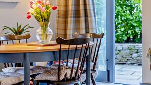 A dining area with a wooden table, two chairs, a vase with flowers, and a view of greenery outside. - 2 Bed in Pentre Bach (oc-b30875) (Pentre-bach)