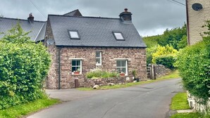 A stone cottage with a sloped roof, two windows with white frames, and a small door. - 2 Bed in Pentre Bach (oc-b30875) (Pentre-bach)