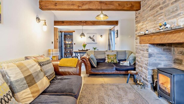 A cozy living room with a stone fireplace, a leather sofa, and a dining area in the background. - 2 Bed in Pentre Bach (oc-b30875) (Pentre-bach)
