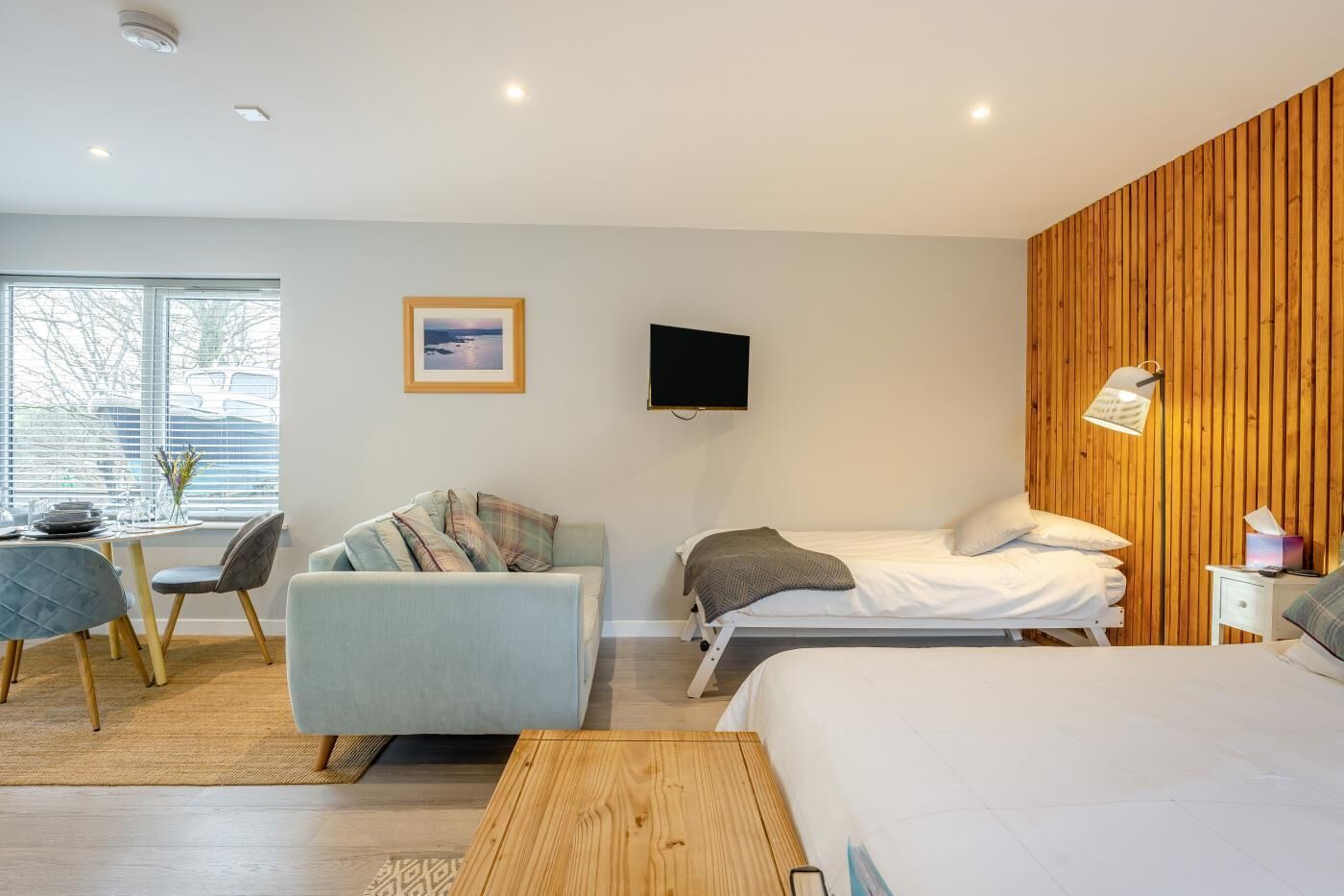 Une chambre moderne avec un lit, un canapé, une télévision et un mur d’accent en bois.