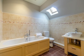 A bathroom with a bathtub, toilet, and sink, featuring beige tiles and a skylight. - 4 Bed in Caistor (oc-t30831) (Caistor)