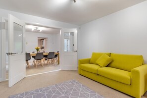 Una sala de estar luminosa con un sofá amarillo y un comedor con mesa y sillas.