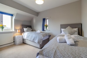 A modern bedroom with two beds, a bedside table, a lamp, and a window with curtains. - 4 Bed in Caistor (oc-t30831) (Caistor)