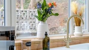 A kitchen counter with a window, a vase with flowers, a bottle of dish soap, and a jar of spices. - 4 Bed in Brecon (oc-h30823) (Brecon)
