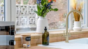 A kitchen counter with a window, a vase with flowers, a bottle of dish soap, and a jar of spices.