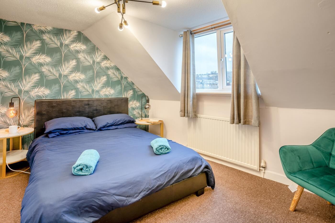 A bedroom with a bed, a nightstand, a lamp, a window, and a green chair.