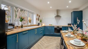 A modern kitchen with blue cabinets, a wooden countertop, and a dining area set for a meal. - 4 Bed in Brecon (oc-h30823) (Brecon)