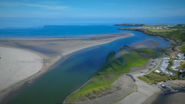 Vista aérea de uma área costeira com praias de areia, uma zona úmida verde e um pequeno povoado com edifícios.