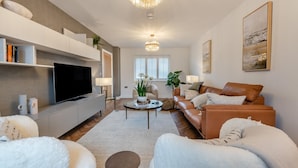 Uma sala de estar moderna com televisão de tela plana, sofá de couro e um grande candelabro.