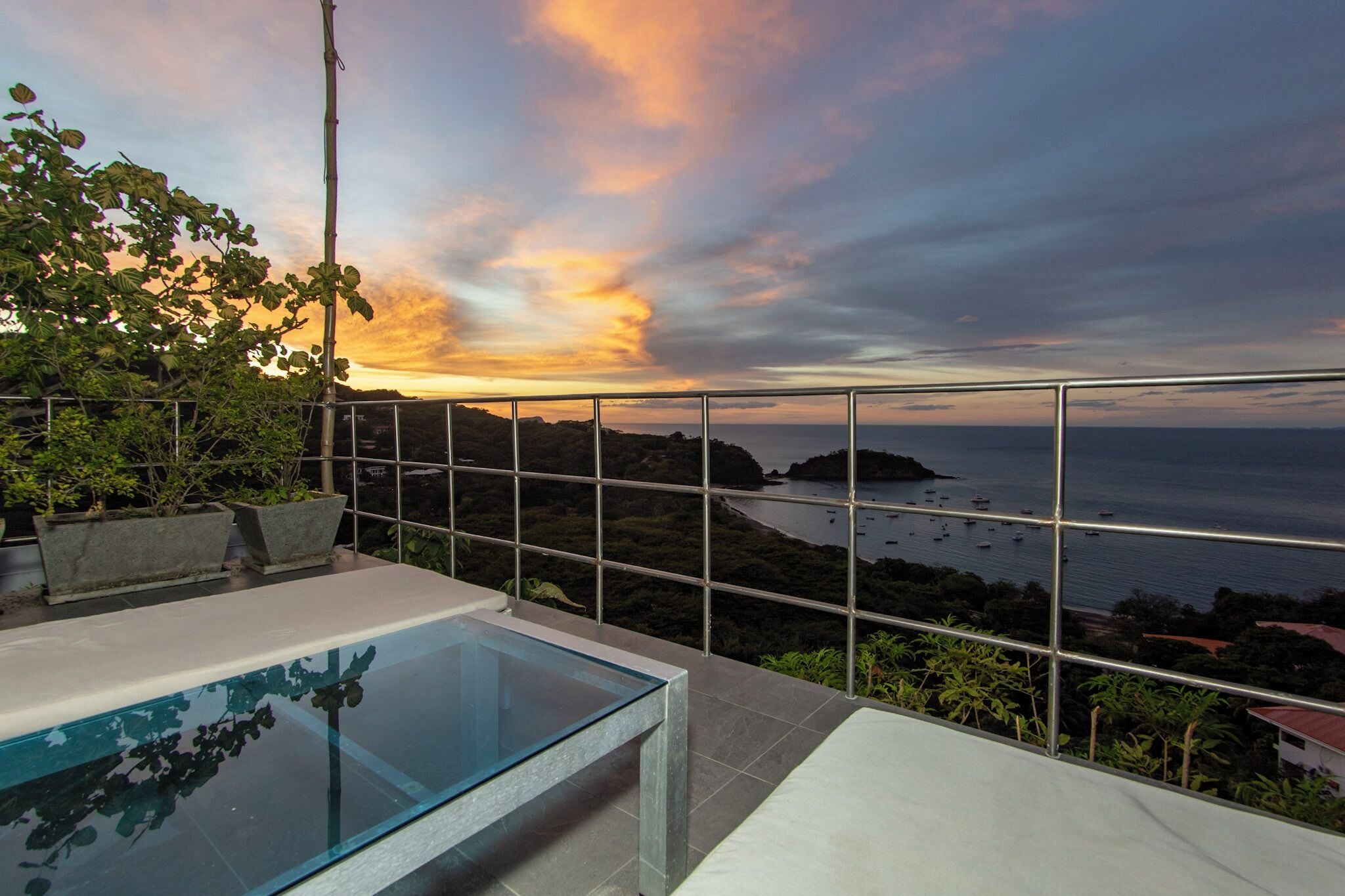 Ein Pool auf dem Dach mit Glasbrüstung und Blick auf das Meer bei Sonnenuntergang.