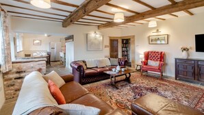 A spacious living room with a brown leather sofa, a red armchair, and a coffee table. There is a patterned rug on the floor, and the room has exposed wooden beams on the ceiling. - 4 Bed in East Morton (oc-t30809) (East Morton)
