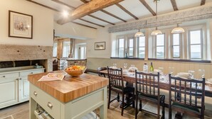 A dining area with a wooden table set for six, a stone fireplace, and a view through large windows. - 4 Bed in East Morton (oc-t30809) (East Morton)