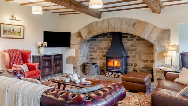 A cozy living room with a stone fireplace, leather sofas, and a television. - 4 Bed in East Morton (oc-t30809) (East Morton)