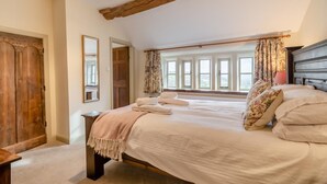 A bedroom with a large bed, wooden beams, a window with curtains, and a mirror on the wall. - 4 Bed in East Morton (oc-t30809) (East Morton)