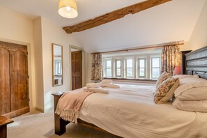 Ein Schlafzimmer mit einem großen Bett, Holzbalken, einem Fenster mit Vorhängen und einem Spiegel an der Wand.