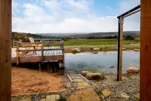 A wooden deck with lounge chairs overlooking a pond and a view of the countryside. - 4 Bed in East Morton (oc-t30809) (East Morton)