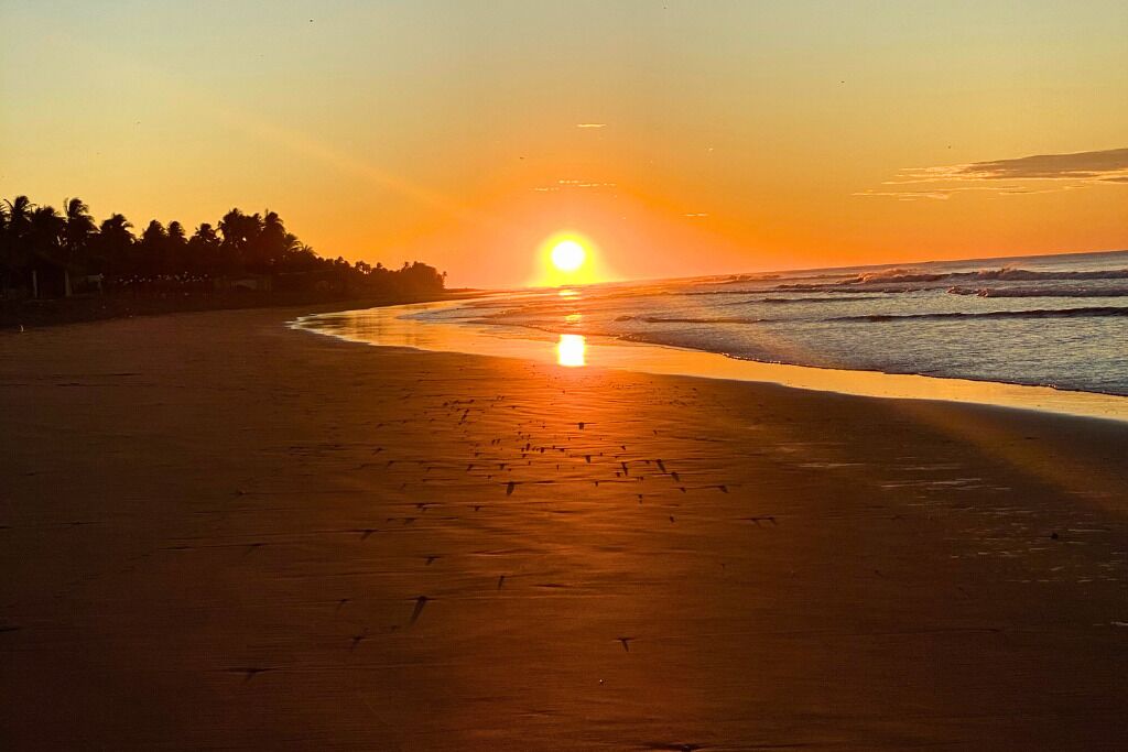 A beach at sunset with a clear sky and calm sea.