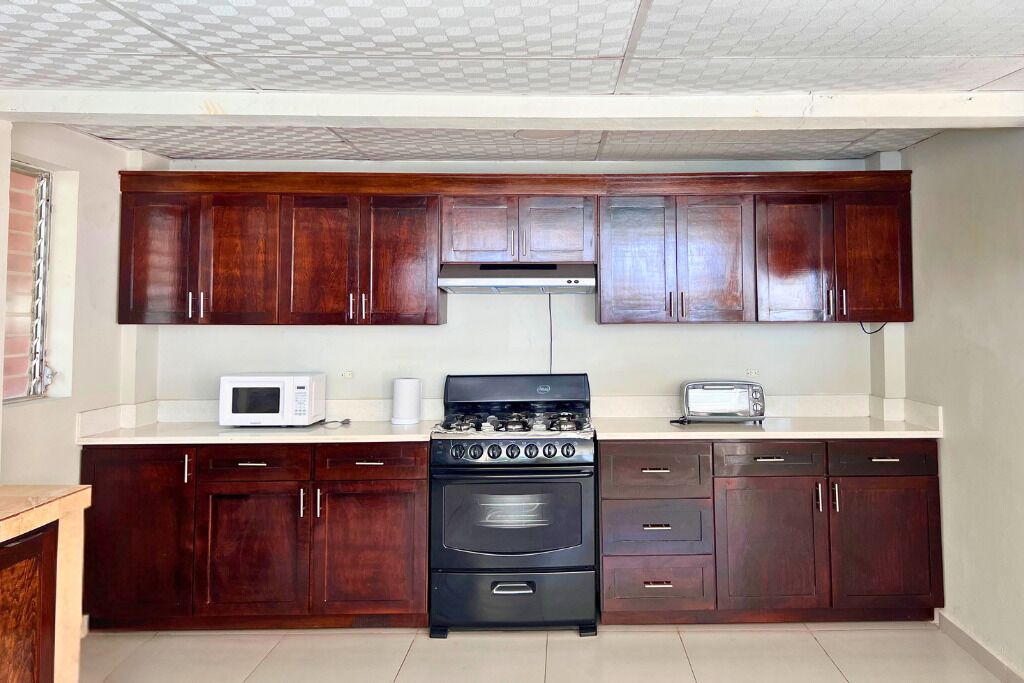 Une cuisine avec des meubles de rangement en bois foncé, une cuisinière noire, un four à micro-ondes blanc et un grille-pain.