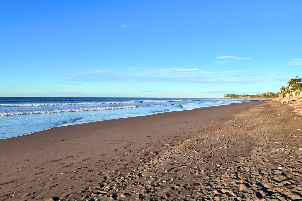 A beach with a clear sky, waves, and a distant shoreline with vegetation.