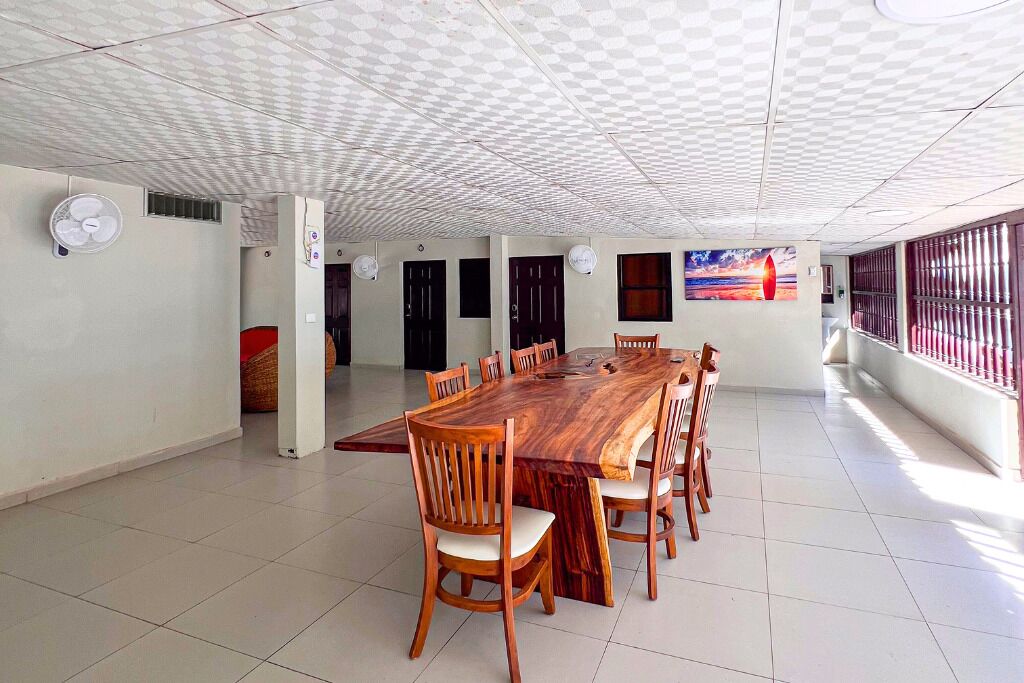 Une pièce spacieuse avec une grande table et des chaises en bois, un plafond décoré et une vue par une fenêtre ornée d’une rambarde en métal.