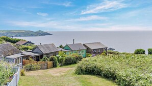 A coastal property with multiple houses, a grassy yard, and a view of the sea and hills in the distance. - 1 Bed in Millbrook (oc-b30672) (Tregonhawke)