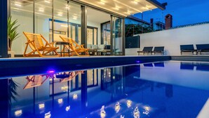 Et moderne poolområde med liggestole og en patio med glas.